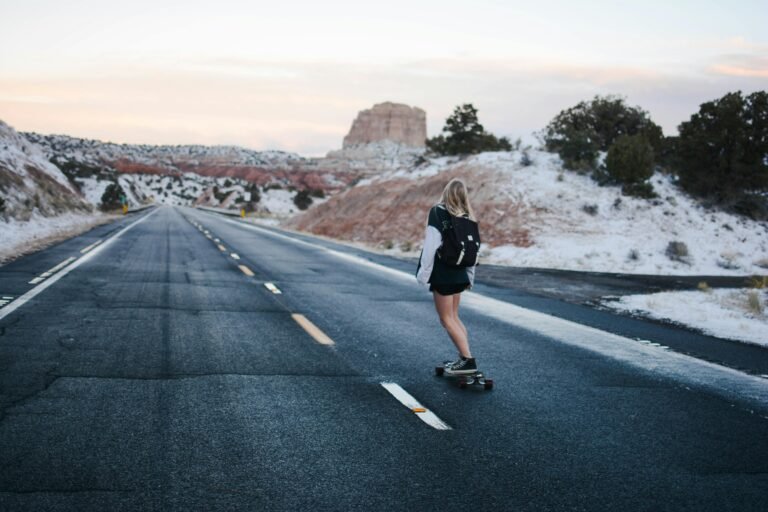 Woman skateboarding down a scenic road with winter backdrop, capturing freedom and adventure.